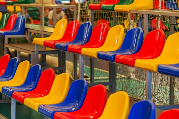 Multicolored Empty plastic chairs in the stands of the stadium. Many empty seats for spectators in the stands. Empty plastic chairs for football fans in the gym. Bright colorful seats for stadium fans