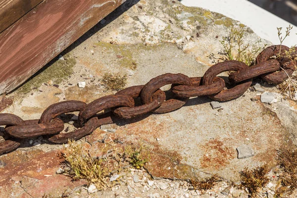 The old rusty metal chain of the anchor of the ship. Giant heavy steel chain leading from land to sea. Yellow mooring line of cargo ship. Ancient rusty Marine anchor chain