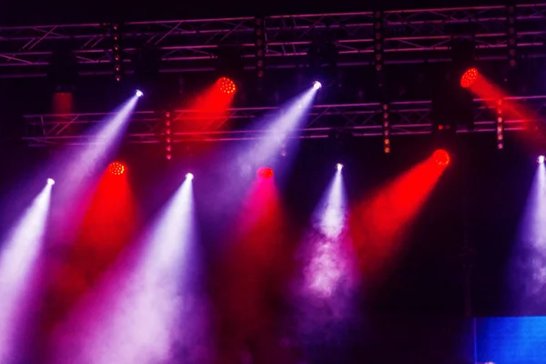 Stage lights. Several projectors in dark. A bright colored spotlight permeates the darkness. Light from the stage, rock concert. Lighting equipment. Several projectors on theatrical lighting system