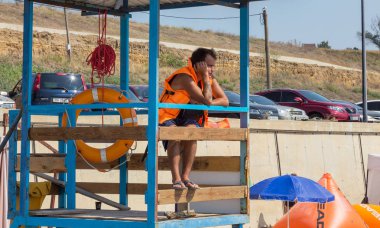 Odessa, Ukrayna - 19 Ağustos 2018: Sahilde bir kule üzerinde bir cankurtaran deniz yıkananlara dışarı bakar. Kurtarıcı turuncu bir hayat şamandıra ile gözlem kulesi, denizin önünde oturur