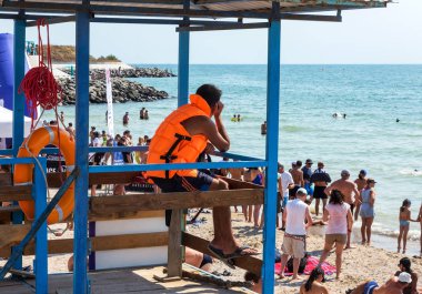 Odessa, Ukrayna - 19 Ağustos 2018: Sahilde bir kule üzerinde bir cankurtaran deniz yıkananlara dışarı bakar. Kurtarıcı turuncu bir hayat şamandıra ile gözlem kulesi, denizin önünde oturur