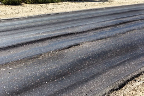 Damaged road, damaged chopped asphalt with potholes and spot. Very bad asphalt road with large trenche. Terrible technology of asphalt production in construction of road. Soft Asphalt melts from heat