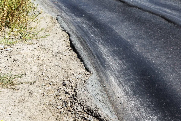 Damaged road, damaged chopped asphalt with potholes and spot. Very bad asphalt road with large trenche. Terrible technology of asphalt production in construction of road. Soft Asphalt melts from heat