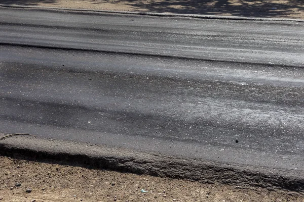 Damaged road, damaged chopped asphalt with potholes and spot. Very bad asphalt road with large trenche. Terrible technology of asphalt production in construction of road. Soft Asphalt melts from heat