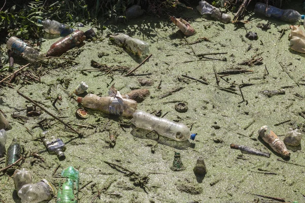 Spilled garbage to small river. Empty used dirty plastic bottles float in canal water. Pollution of environment by household waste. Ecological problem. River contaminated with various garbage