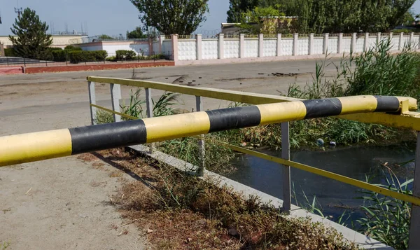 Old and rusty car barrier on the road to the private office area. Iron yellow-black blocking the road to road transport barrier. Barrier of private property