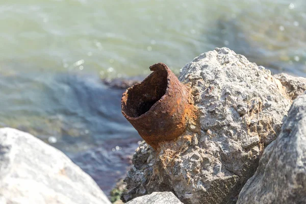 A piece of truncated, broken off rusty pipe sticks out of a piece of concrete. Metal rust is a broken construction. A piece of Rusty pipe on the sea-line. Building debris thrown ashore