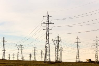 Yüksek gerilim hatları ve güneşli bir düz ve yeşil tarım peyzaj güç pilonlar mavi gökyüzünde cirrus bulutlar ile. Pilon ve iletim güç hattı 