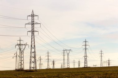 Yüksek gerilim hatları ve güneşli bir düz ve yeşil tarım peyzaj güç pilonlar mavi gökyüzünde cirrus bulutlar ile. Pilon ve iletim güç hattı 