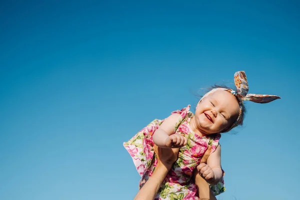 Baba a levegőben. Vidám gyermek kék ég háttér. Egy kislány kezén, aki felhőkben repül. Divatgyermek fejfedővel Stock Fotó
