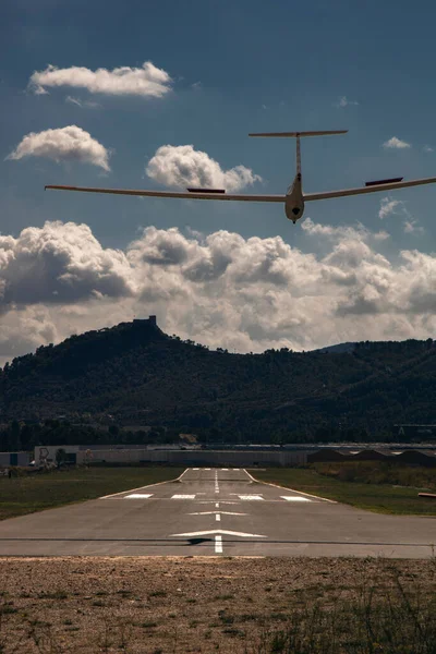 Landscape showing a plane landing on a landing track in a small aerodrome and some mountains under a cloudy sky