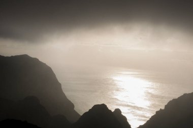 Kayalık bir sahil ve Tenerife adasında gün batımında okyanusun siyah beyaz görüntüsü