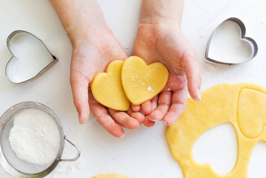 closeup girl holding raw dough of  heart shape cookies for baking