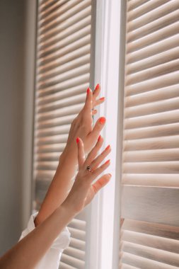 Pencerenin arka planında bir kadın eli. Bir kadın evde yatakta gerinerek uyanıyor. Sabah erkenden kalkıp güneşli bir günde uyanmak. Yaşam Tarzı Konsepti