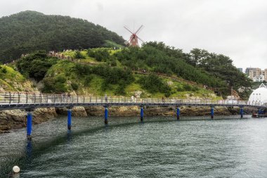 Liman bölgesinden rüzgârlı tepeler görünüyor. Yel değirmeni bölgesine doğru yürüyen bir grup turist. Geoje, Güney Kore 'de çekildi.