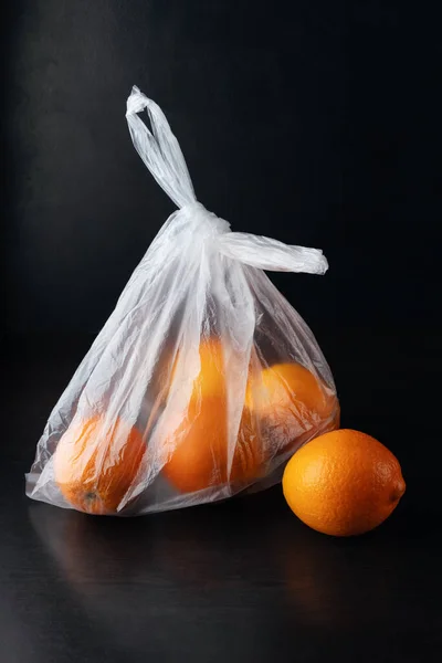 Siyah arka planda plastik poşetteki portakallar. Sosyal içerik.