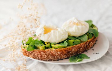 Tam tahıllı ekmek, avokado, roka ve küçük çingene çiçekleriyle süslenmiş nigella serpiştirilmiş haşlanmış yumurtalı sandviç. Tekstil ve bej arka plan. Boşluğu kopyala