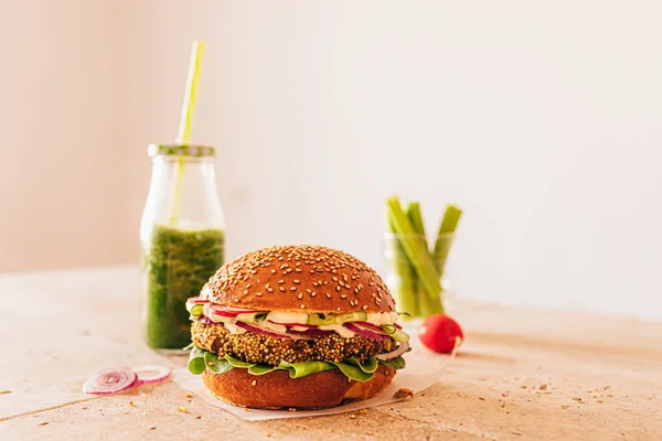 Bir şişe yeşil smoothie ile vejetaryen burger ve bardakta kerevizli havuç. Taş bej masa