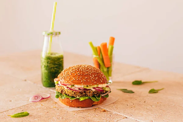 Bir şişe yeşil smoothie ile vejetaryen burger ve bardakta kerevizli havuç. Taş bej masa