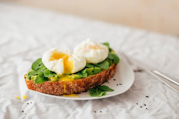 Tam tahıllı ekmek, avokado, roka ve küçük çingene çiçekleriyle süslenmiş nigella serpiştirilmiş haşlanmış yumurtalı sandviç. Tekstil ve bej arka plan. Boşluğu kopyala