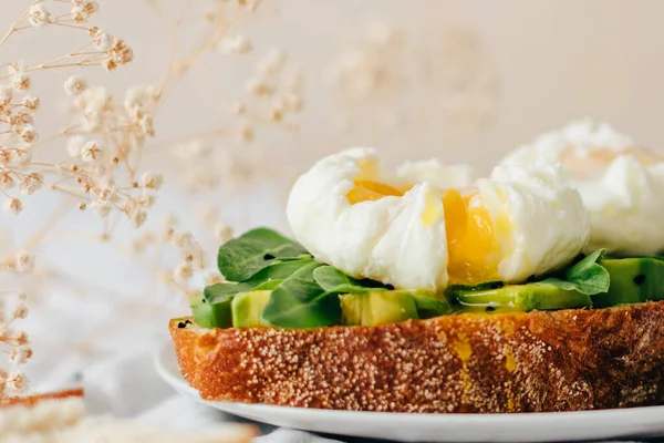 Tam tahıllı ekmek, avokado, roka ve küçük çingene çiçekleriyle süslenmiş nigella serpiştirilmiş haşlanmış yumurtalı sandviç. Tekstil ve bej arka plan. Uzayı kopyala Kapat.