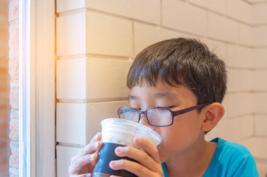 Genç yakışıklı çok güzel Asyalı çocuk içecek sütlü tadına bir kafede cam.