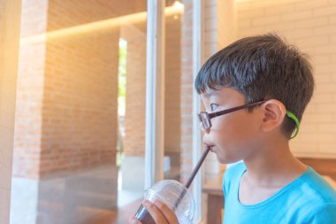 Genç yakışıklı çok güzel Asyalı çocuk tadına bir kafede ile tarafından plastik saman süt emmek.