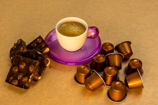 Cup of coffee on a beige background with pieces of chocolate and coffee capsules. Sweet food. Healthy breakfast. — Stock Photo, Image