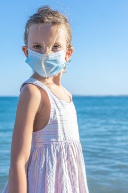 Sahilde koruyucu maske takan bir kız.