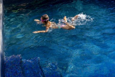 Küçük kız mavi yüzme havuzunda yüzüyor. Kaliteli fotoğraf