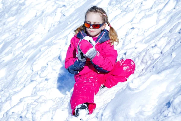 Giovane ragazza seduta sulla montagna di neve e giocare con la palla di neve . — Foto Stock