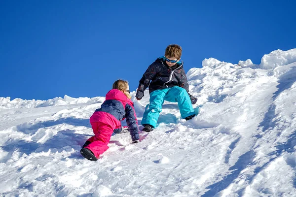 Duas crianças alegres brincando na montanha nevando em um dia de inverno . — Fotografia de Stock