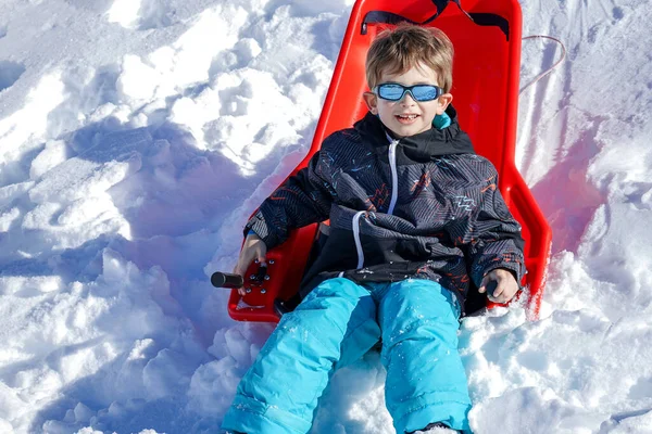 Rapaz sentado no trenó vermelho na montanha de neve — Fotografia de Stock