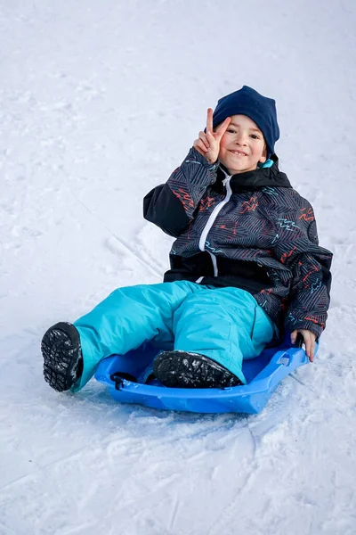 Junge sitzt auf dem blauen Schlitten auf dem Schneeberg — Stockfoto