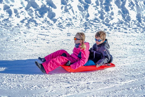 Dos niños felices bajando en trineo por las colinas en un día de invierno. — Foto de Stock