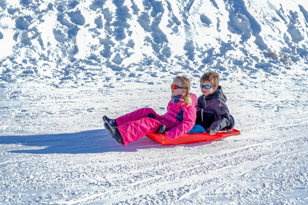 Due bambini gioiosi slittano giù per le colline in una giornata invernale. — Foto Stock