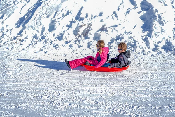 Due bambini gioiosi slittano giù per le colline in una giornata invernale. — Foto Stock