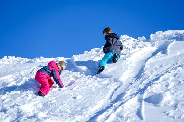 Duas crianças alegres brincando na montanha nevando em um dia de inverno . — Fotografia de Stock