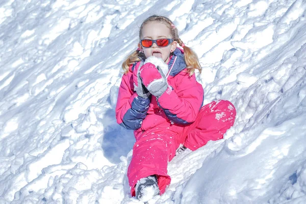 Giovane ragazza seduta sulla montagna di neve e giocare con la palla di neve . — Foto Stock
