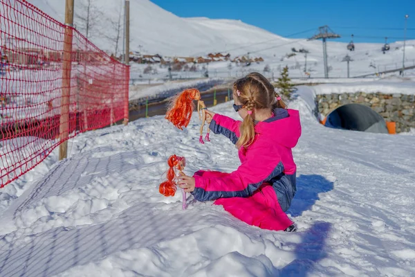LAlpe DHuez, Γαλλία 30.12.2019 Υπαίθριο χειμερινό πορτραίτο μικρού χαριτωμένου κοριτσιού με γυαλιά ηλίου και ρούχα για σκι. Κορίτσι που παίζει με κούκλες. — Φωτογραφία Αρχείου