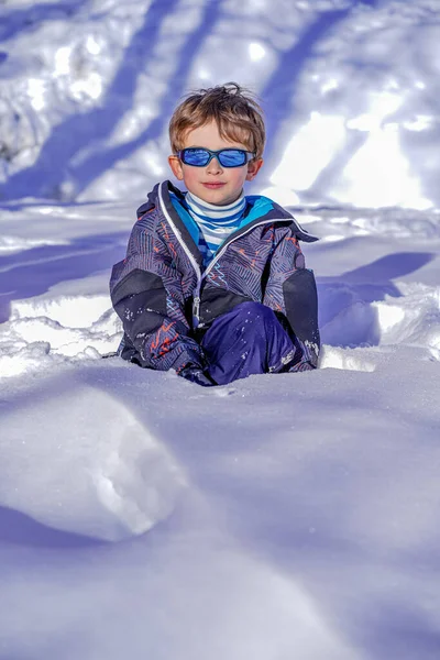 Mjuk fokus bakgrund. Ung pojke med solglasögon leker i snön — Stockfoto