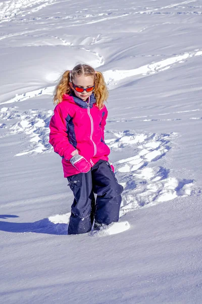 Concentração suave. Menina bonita vestindo uma jaqueta de esqui rosa jogando e correndo em um parque de inverno nevado. — Fotografia de Stock