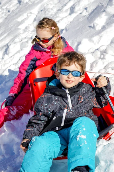 Duas crianças alegres brincando na montanha nevando em um dia de inverno . — Fotografia de Stock