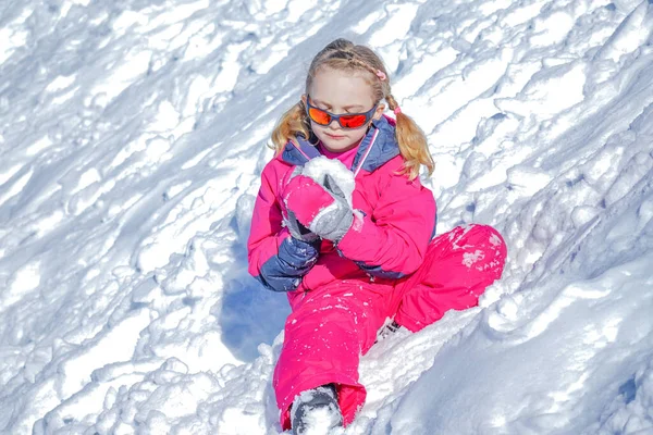 Giovane ragazza seduta sulla montagna di neve e giocare con la palla di neve . — Foto Stock