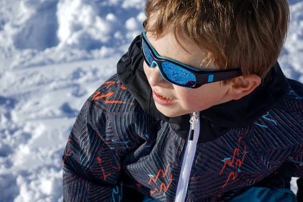 Κοντινό πλάνο του νεαρού αγοριού με τα γυαλιά ηλίου που κάθεται στο χιόνι — Φωτογραφία Αρχείου