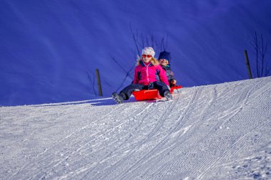 Yumuşak odak arkaplanı. Bir kış günü tepelerden kayan iki neşeli çocuk..