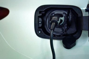 Aküyü şarj etmek için güç kaynağı elektrikli araca bağlanıyor. Otomobilin gelecekteki taşıma teknolojisi yükleniyor. Lüks beyaz elektrikli araba şarj oluyor.. 