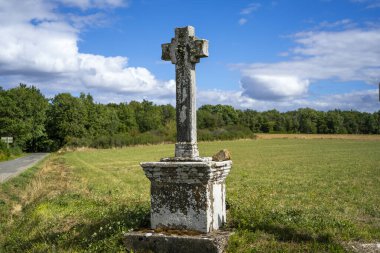 Eski taş gri haç, arka plandaki yeşil orman ve tarlanın kavşağında duruyor.. 