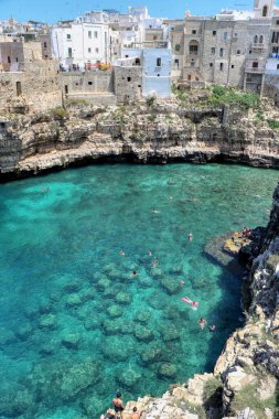 Polignano a Mare, Puglia, İtalya 'nın ünlü Lama Monachile plajındaki mavi denizin kayalıklarında hamamlar ve turistler