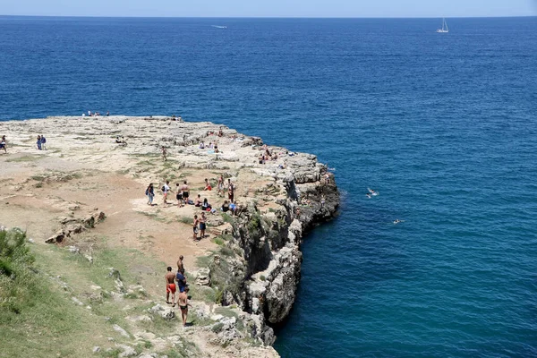Polignano a Mare, Puglia, İtalya 'nın ünlü Lama Monachile plajındaki mavi denizin kayalıklarında hamamlar ve turistler
